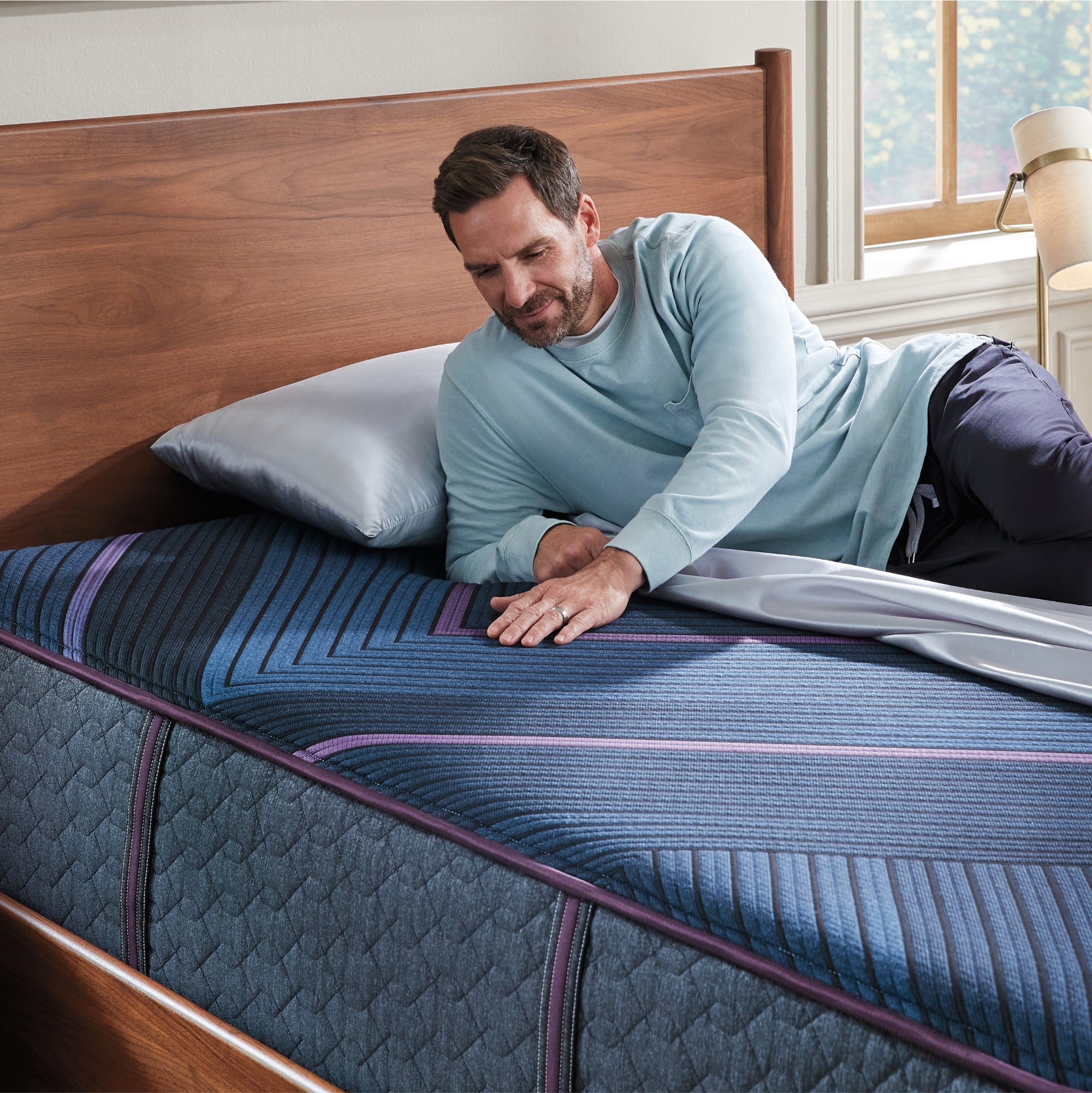 Man laying on a World Class Hybrid mattress on his right side rubbing his left hand on the top of the mattress.